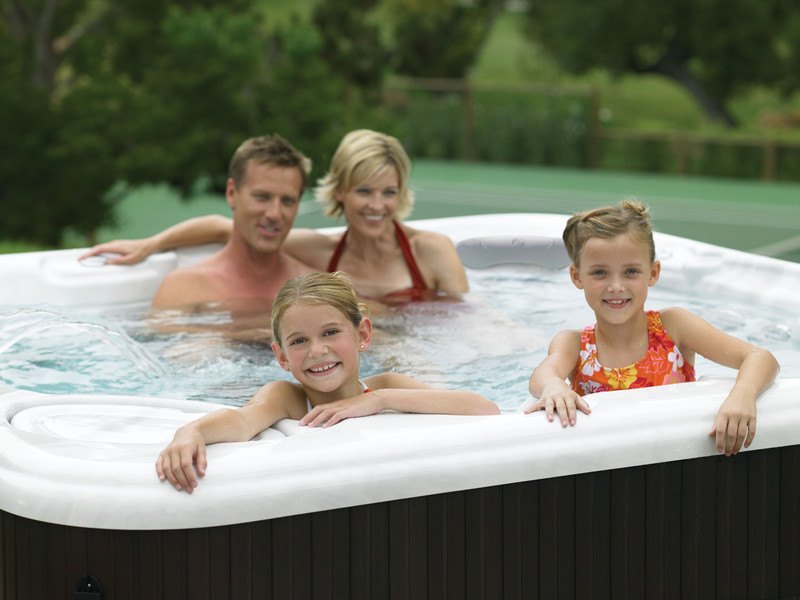 A family of four relaxes and smiles in a luxurious salt water hot spring spa tub. The salt water is gentle on their eyes and skin, providing a soothing and rejuvenating experience.