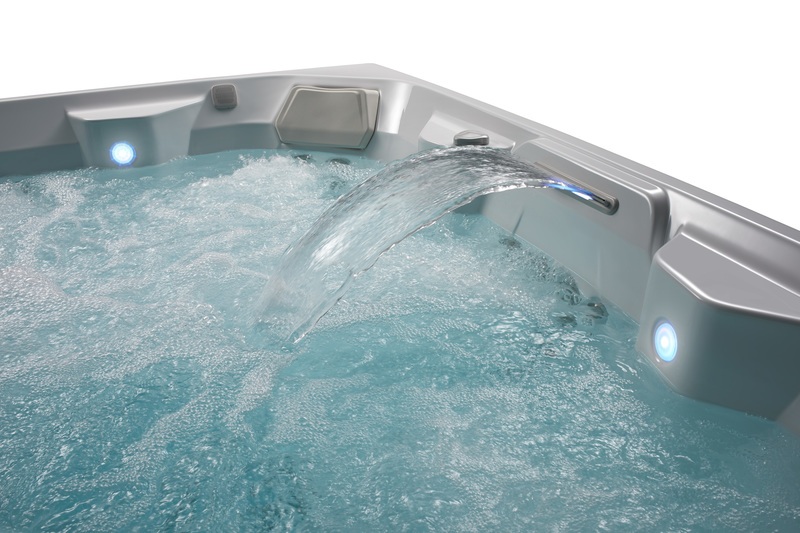 A close-up of a hot tub with a cascading waterfall feature and blue LED lights.
