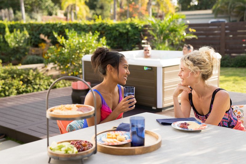 A couple of friends having lunch by a Limelight Flair hot tub.