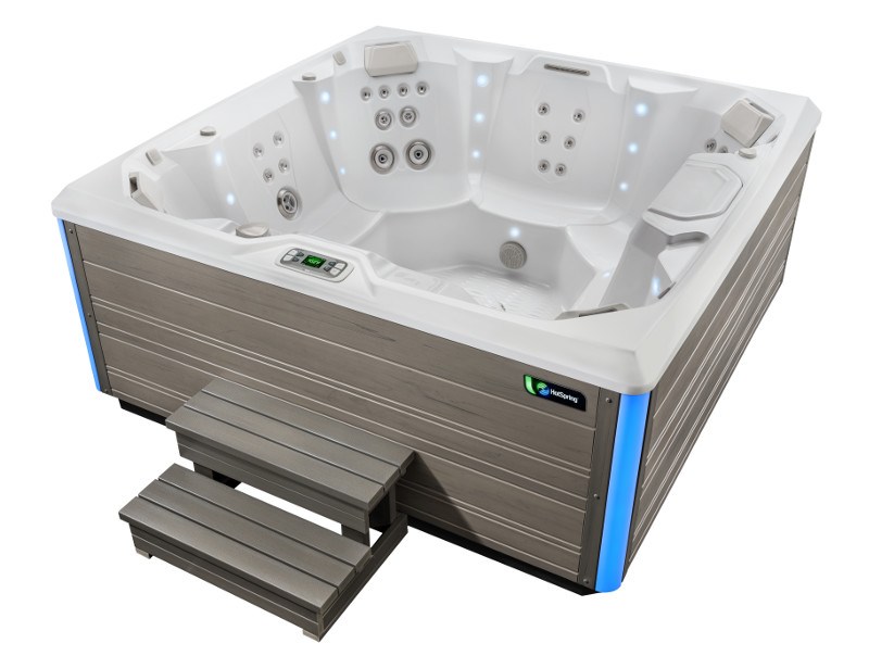 A Hot Spring Spa hot tub with blue LED lights featuring multiple jets and a wooden step stool.
